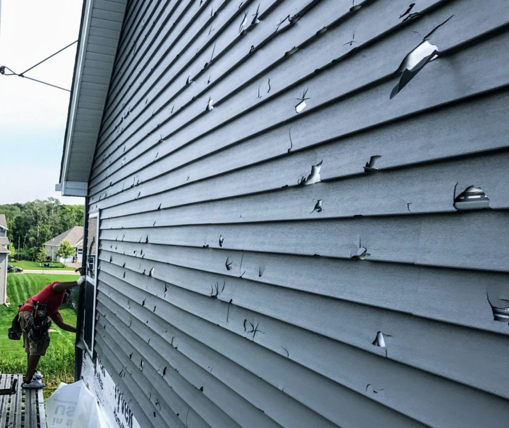 damaged home siding with holes from a severe storm